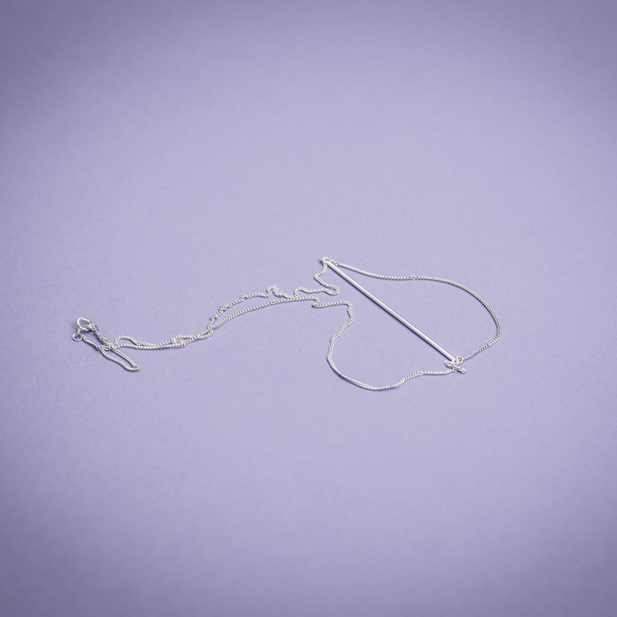 3. Flat lay of Maarja Palu Necklace SWING in silver on purple background, highlighting chain and bar design