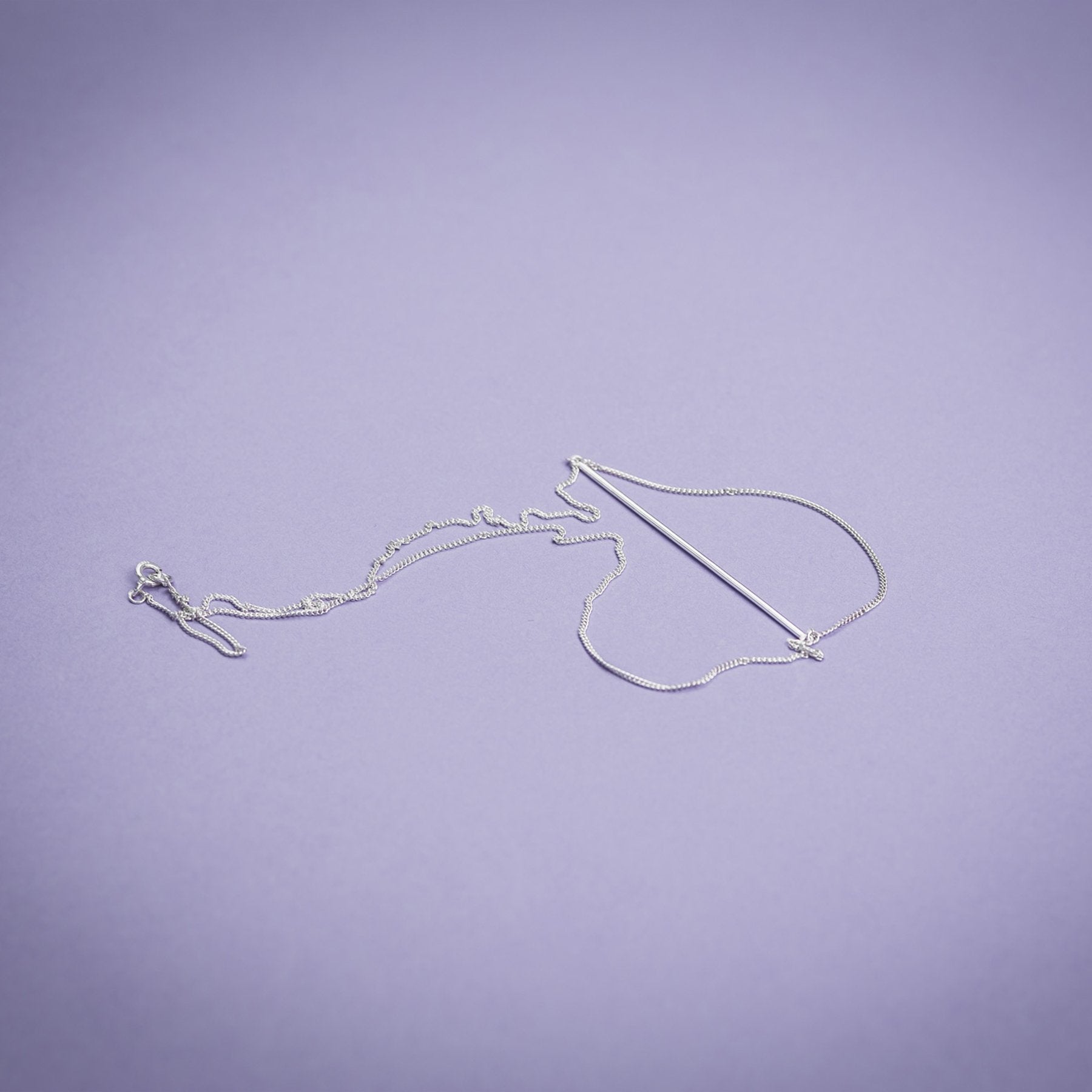 3. Flat lay of Maarja Palu Necklace SWING in silver on purple background, highlighting chain and bar design