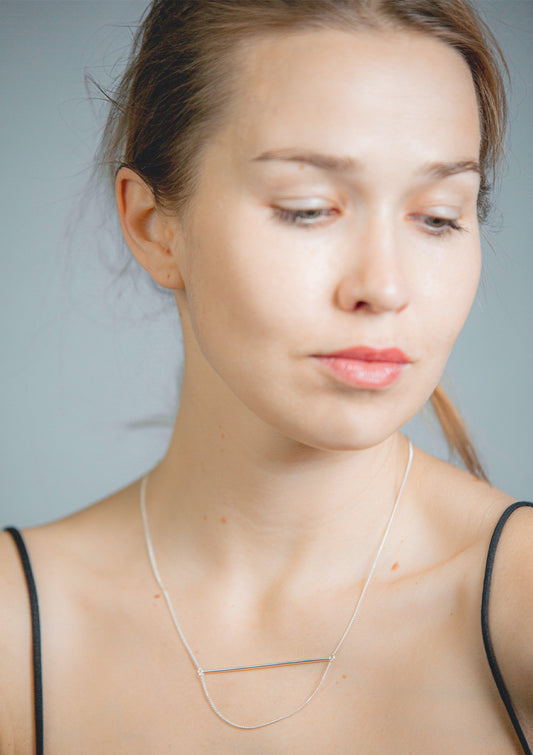 1. Woman wearing Maarja Palu Necklace SWING in silver, showcasing minimalist geometric design