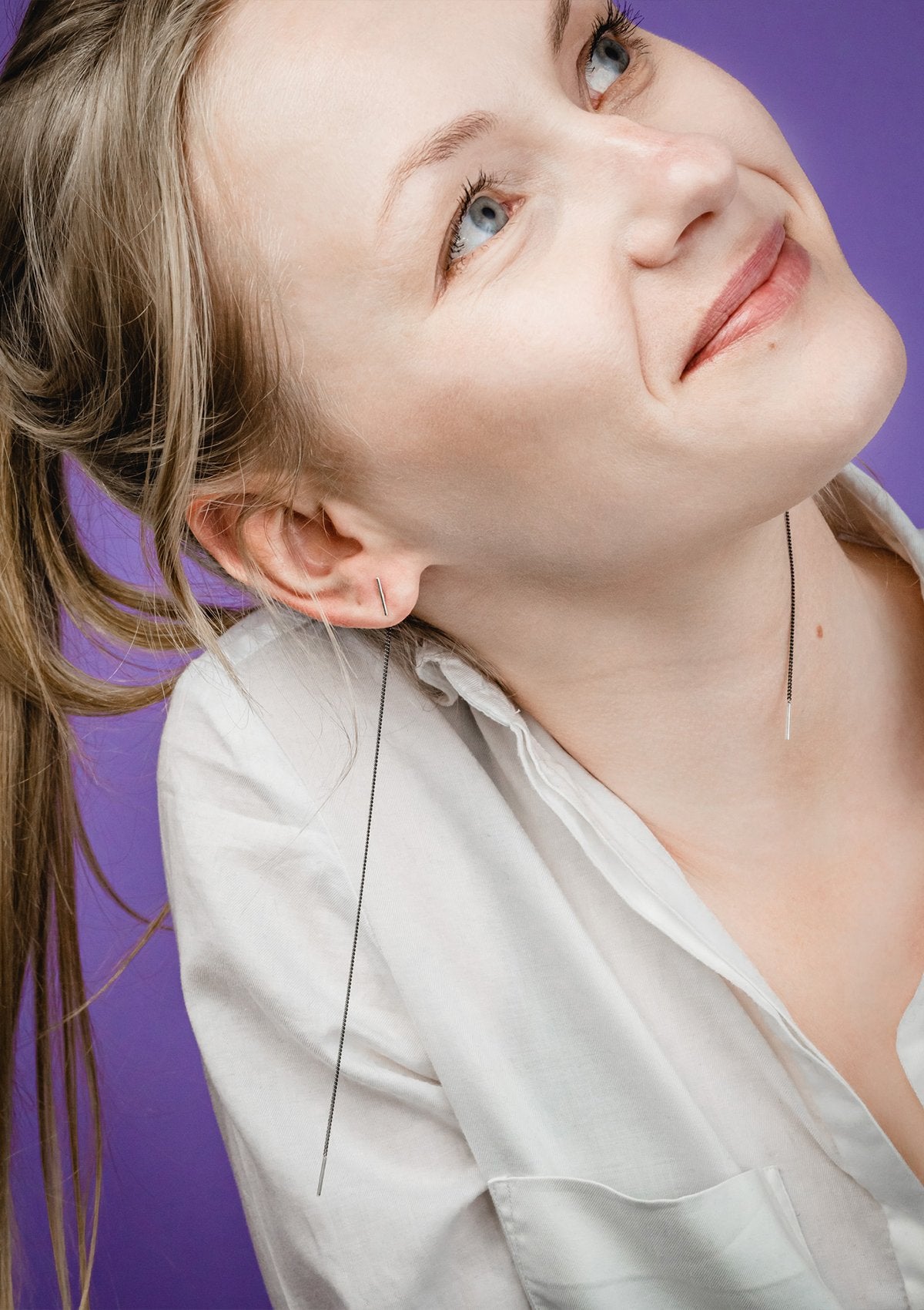 1. Woman wearing Maarja Palu SWING 2 earrings with long silver chains, shown in lifestyle setting