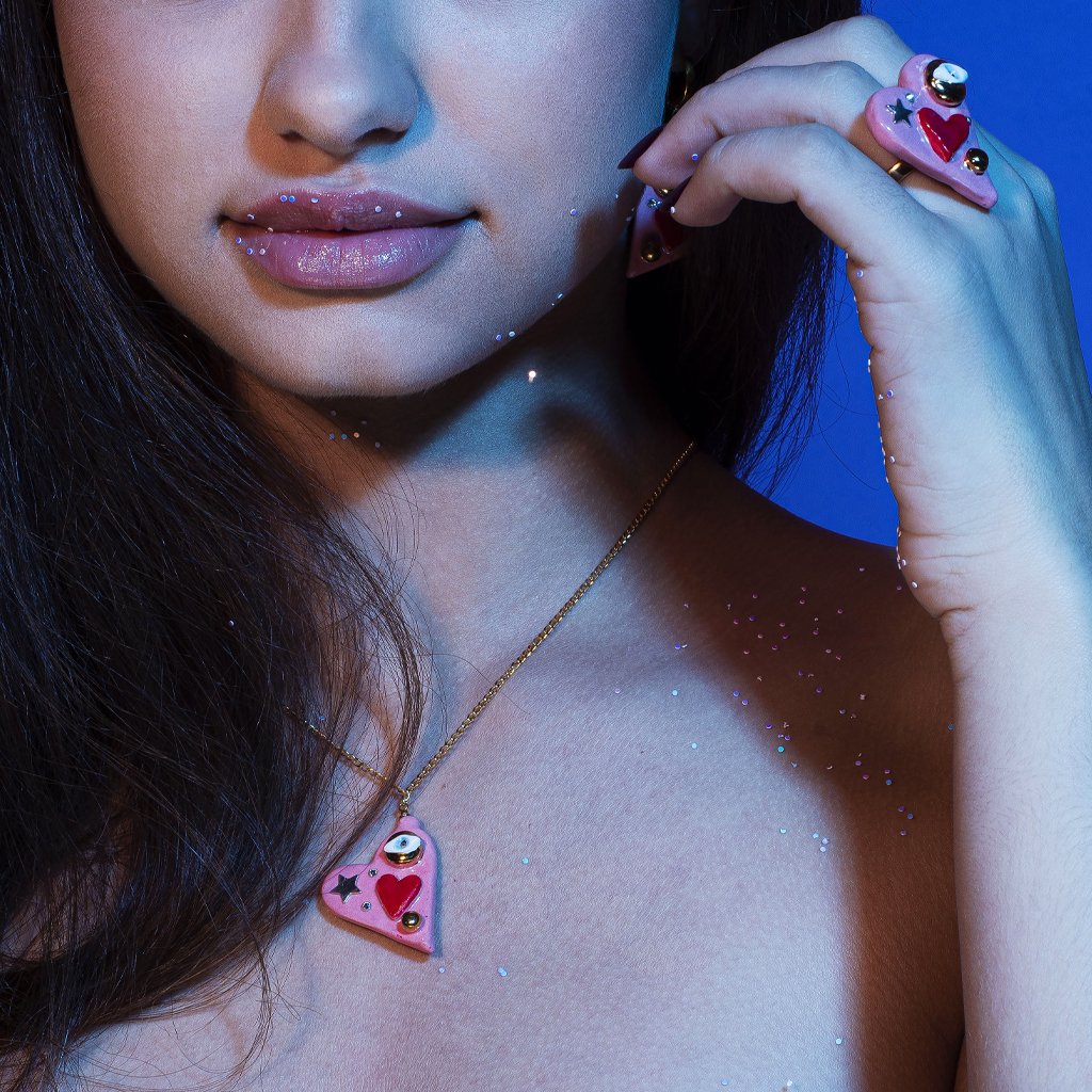 2. Woman wearing SCULP All You Need Is Love necklace with ceramic heart pendant and matching ring, shown in lifestyle setting