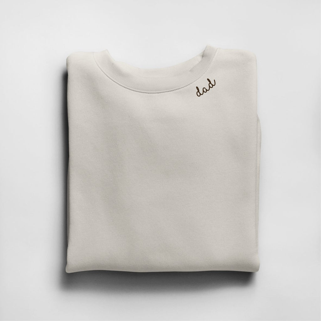 3. Beige unisex organic cotton sweatshirt with 'dad' embroidery, folded in studio setting