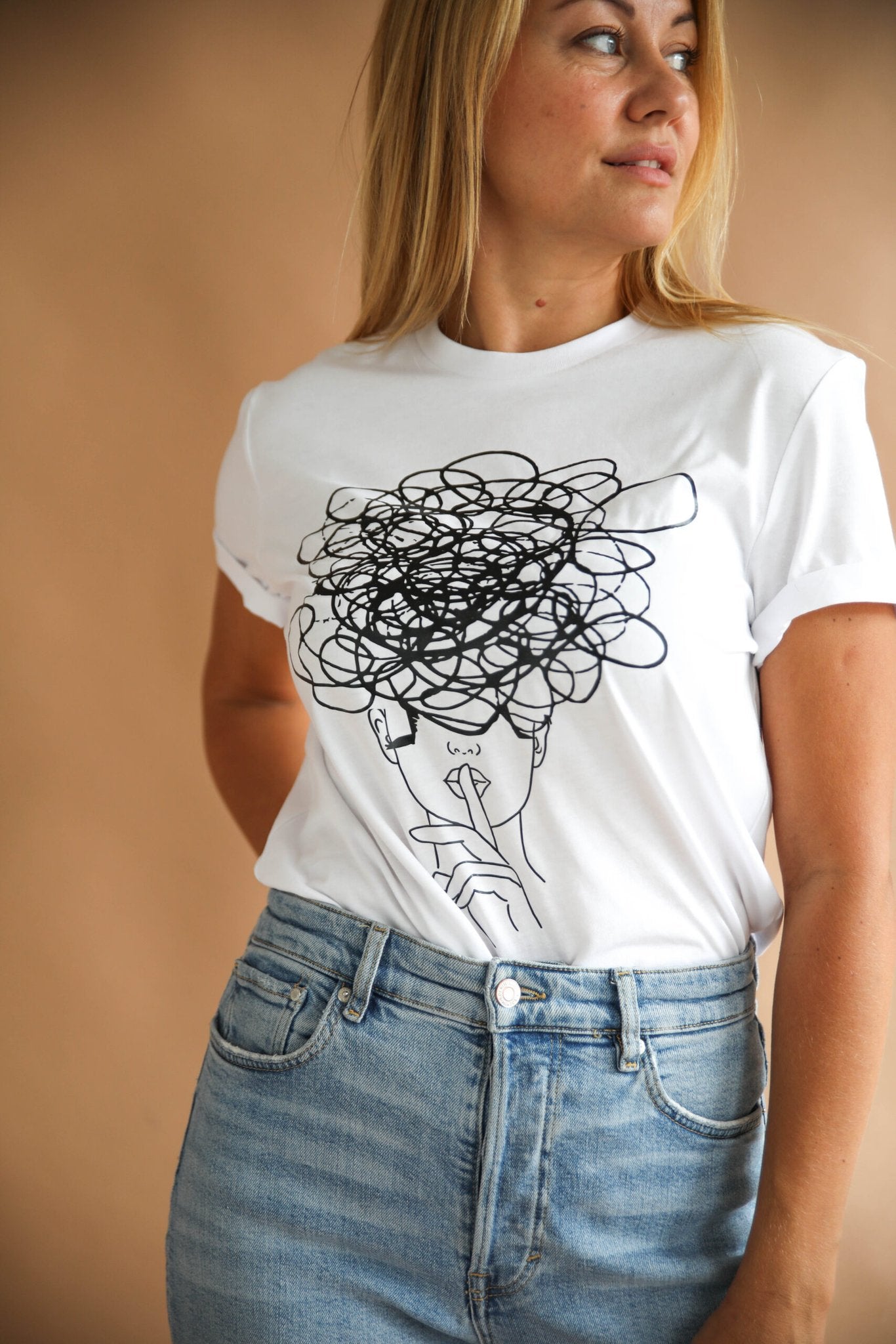 1. Women's white Šššhhh! T-shirt by Black Giraffe Brand with abstract face design, worn with rolled-up sleeves in lifestyle setting