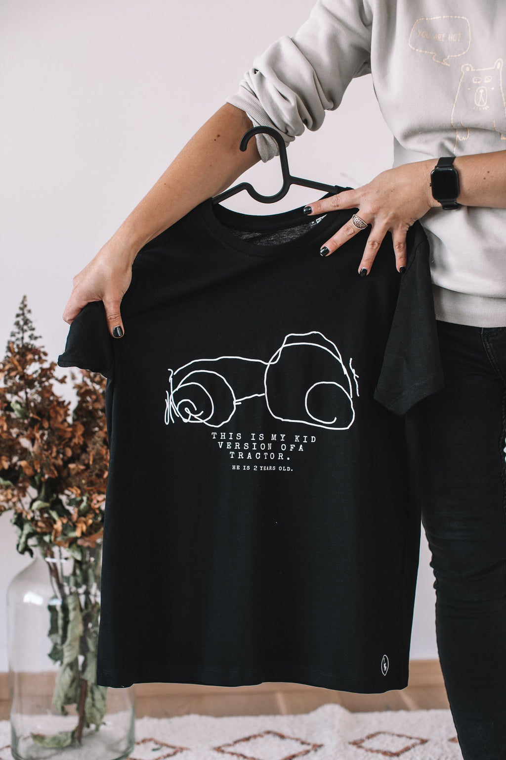 3. Black Giraffe Brand black T-shirt with child's drawing of abstract shapes and text, held by a person in a casual setting