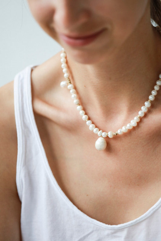1. Woman wearing New Vintage by Kriss custom-made pearl necklace with Baroque pearls and gold-filled details, styled with a white top