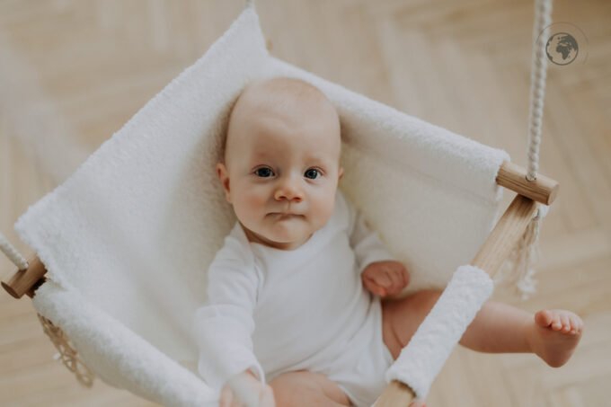 2. Baby sitting in bouclé snow white swing with oak wood poles, smiling in a bright room