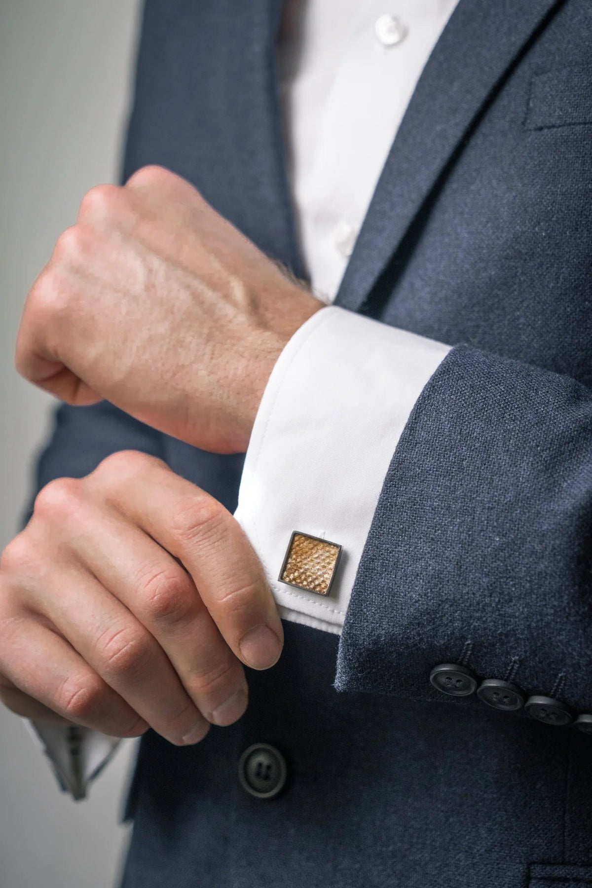 2. Man adjusting white shirt cuff with yellow leather square cufflink by Eherüs, wearing a dark suit