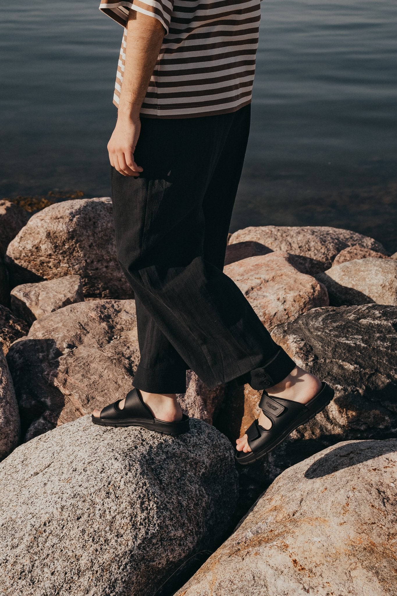 2. Close-up of men's Madise Sandals in black on rocks, highlighting adjustable velcro straps