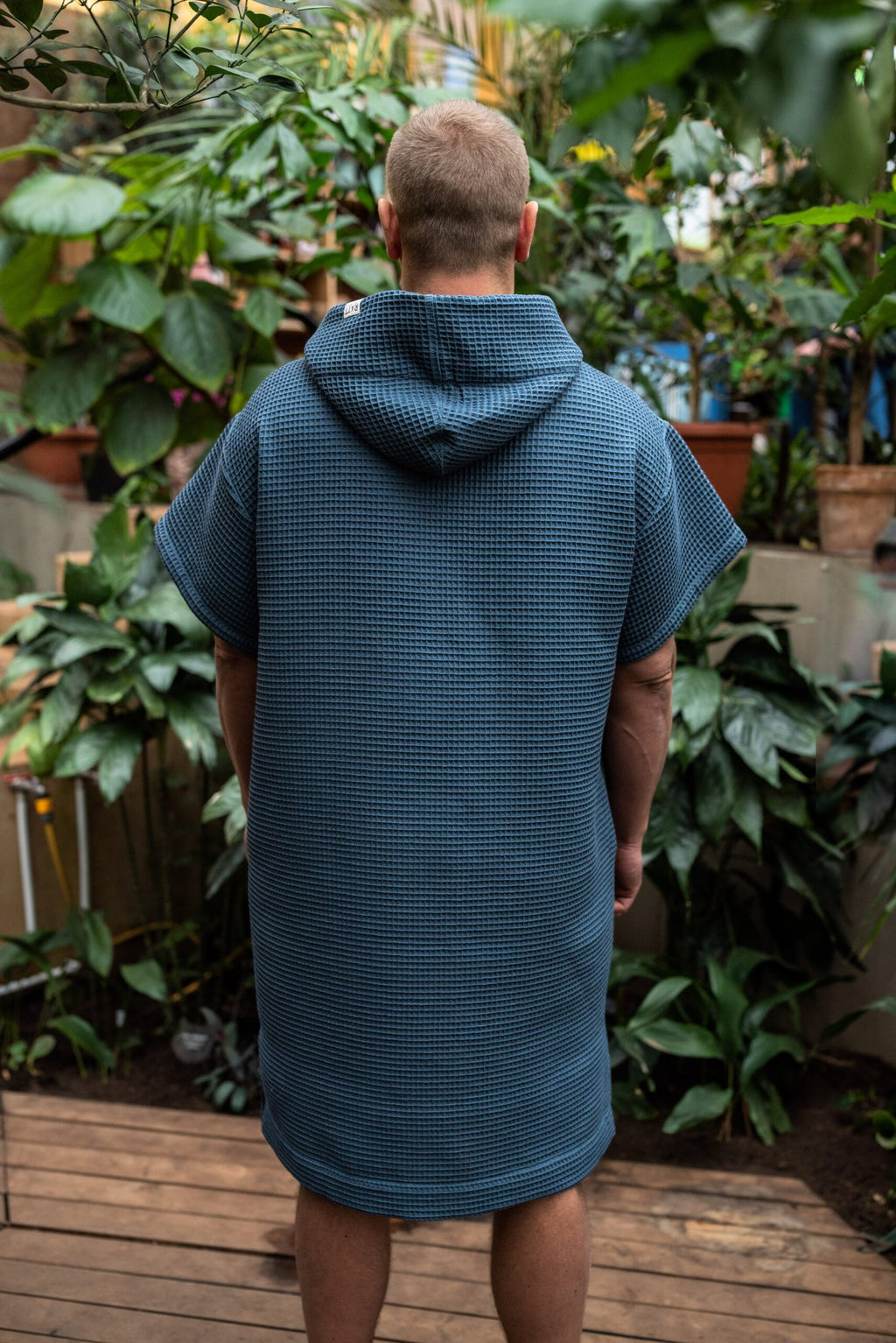 13. Man wearing blue RÄTT short-sleeve surf poncho with hood, shown from the back