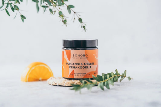 2. BONOBO orange and carrot body scrub jar on woven mat with orange slice and greenery, studio setting