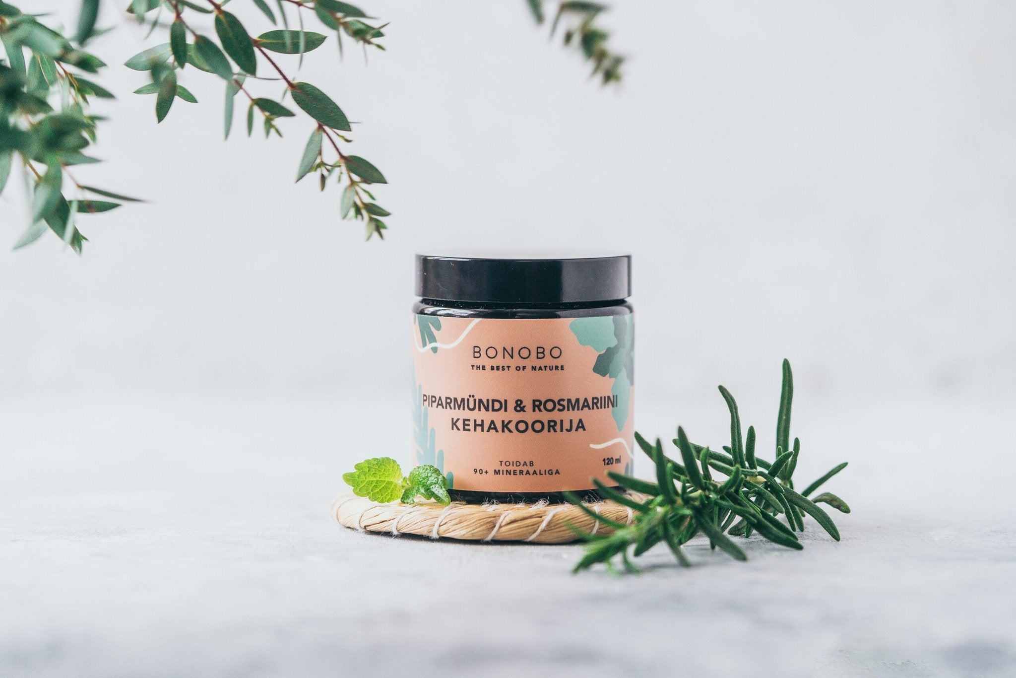 3. BONOBO body scrub jar with peppermint and rosemary, displayed with fresh herbs on woven mat