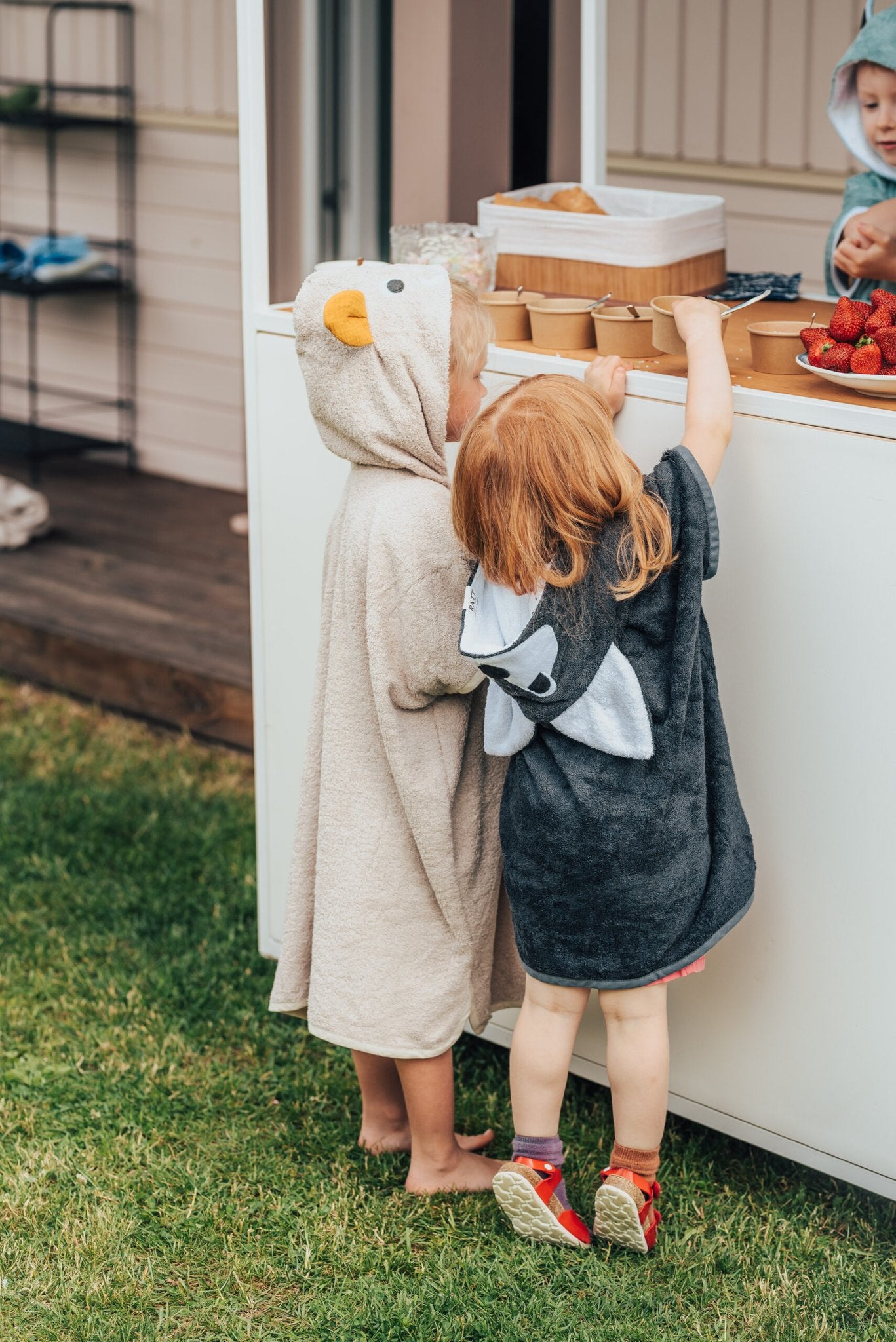 3. Back view of child in RÄTT Short-Sleeve Poncho WOLF, showing wolf design hood