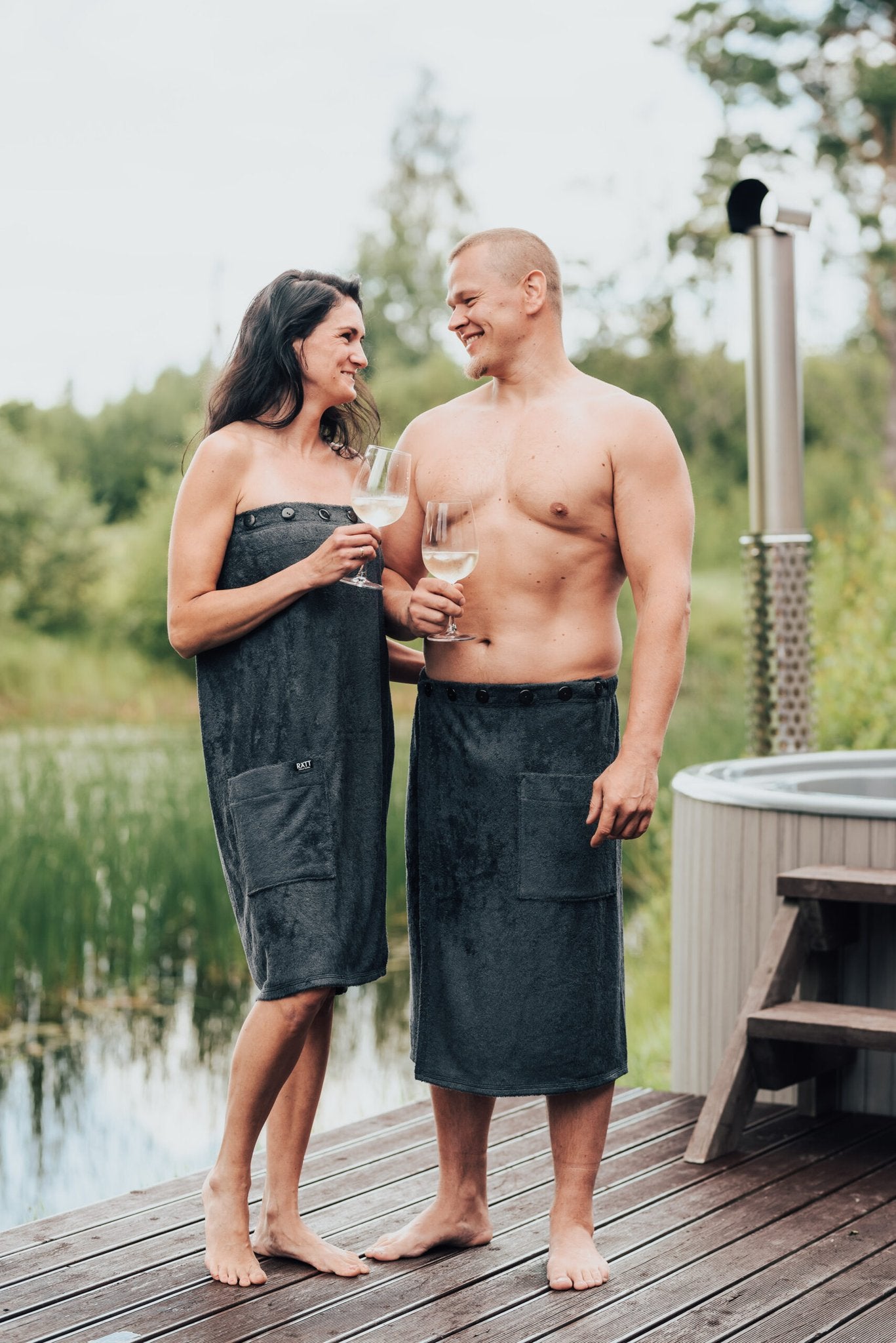 1. Men's dark grey bamboo terry spa wrap by RÄTT, worn by male and female models outdoors near a hot tub