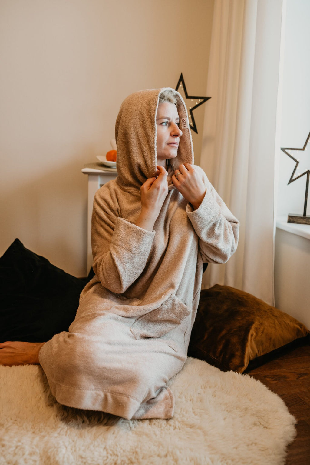 3. Women's beige bamboo terry long-sleeve poncho with hood, worn by model sitting indoors on a rug