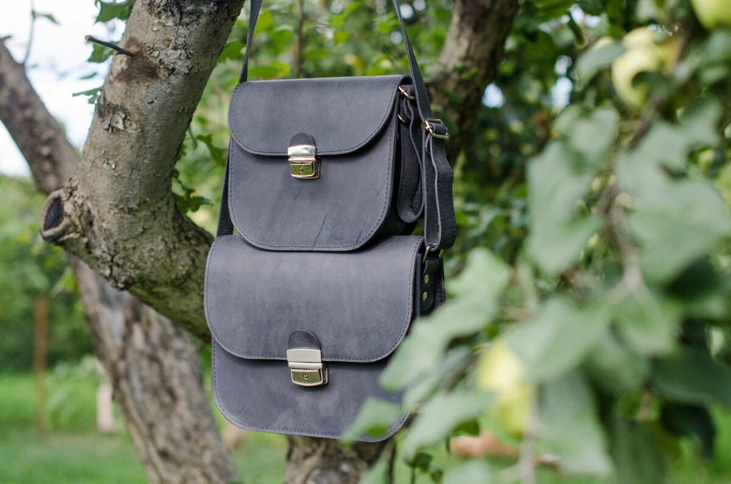 10. Woman wearing Zelma Kraft grey leather saddle bag with adjustable strap, styled with white blouse