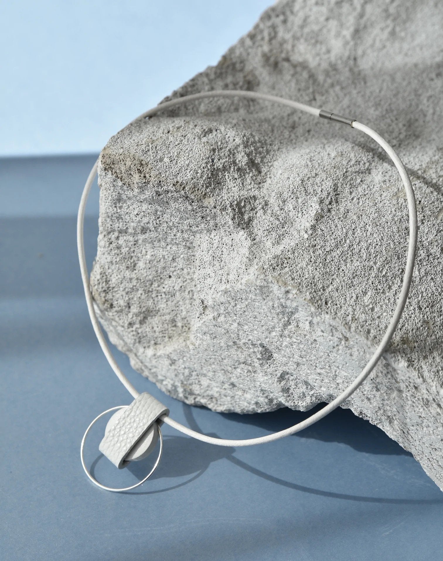 3. Studio shot of Gerda Retter Design Luce Mini Handmade Necklace in white, featuring geometric pendant and silver accents on textured background