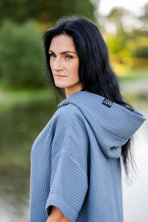 5. Woman in blue RÄTT short-sleeve surf poncho with hood, standing by a lake