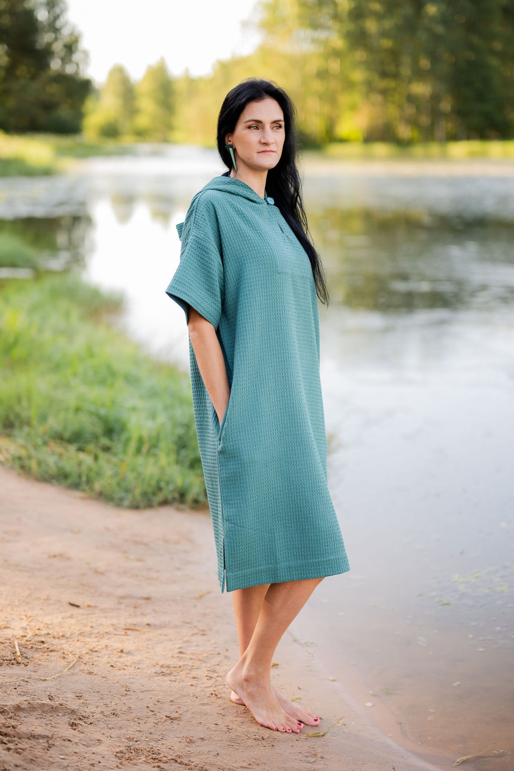 10. Woman standing by water in teal RÄTT short-sleeve surf poncho with hood