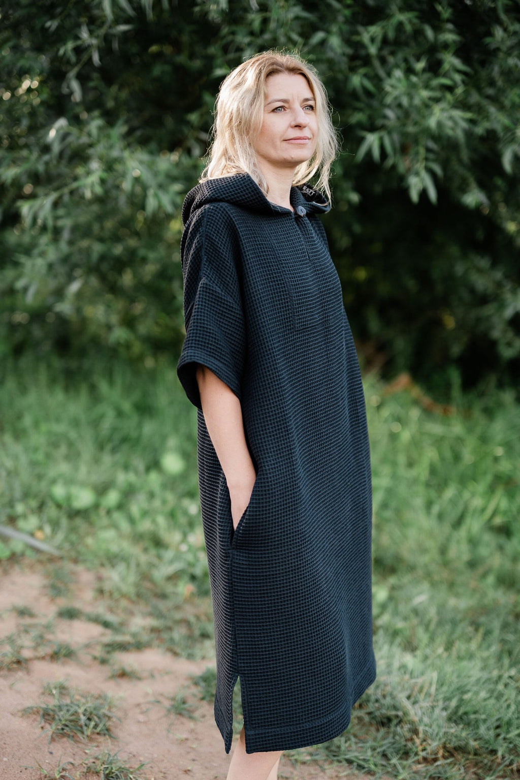 9. Woman standing in black RÄTT short-sleeve surf poncho with hood, side view