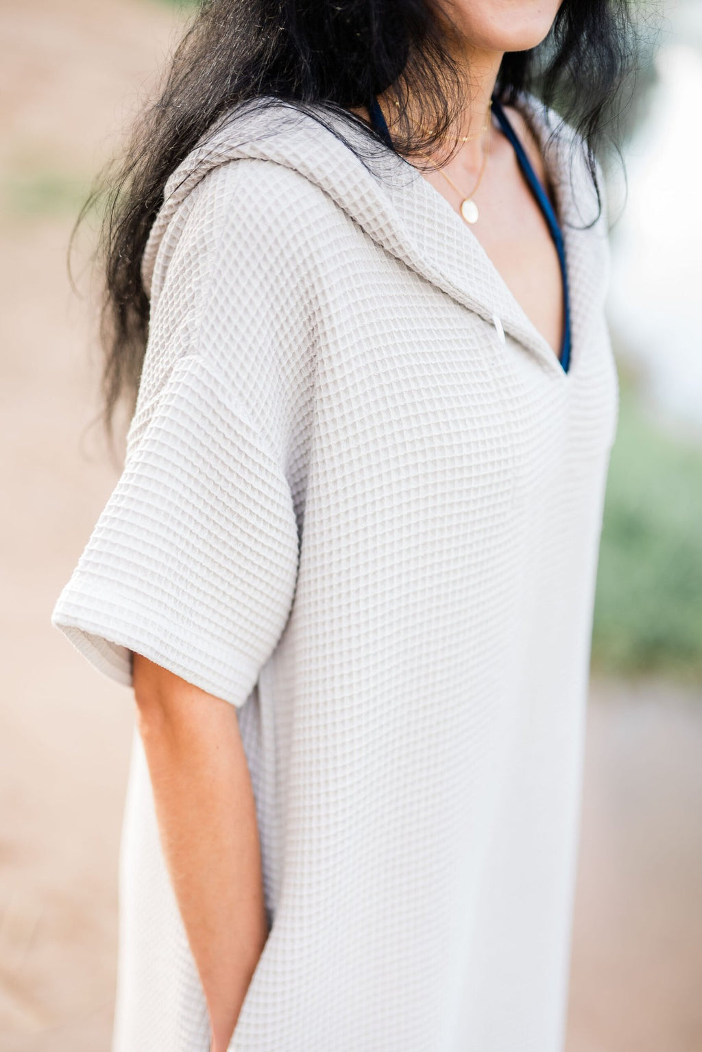 7. Close-up of woman in light grey RÄTT short-sleeve surf poncho, showing texture and hood