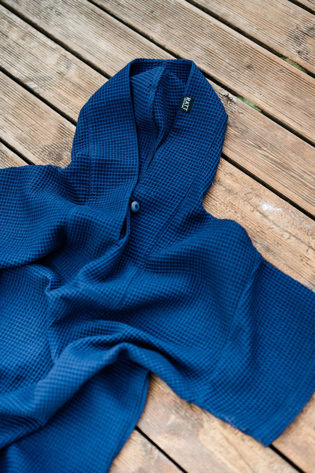 14. Flat lay of blue RÄTT short-sleeve surf poncho on wooden surface