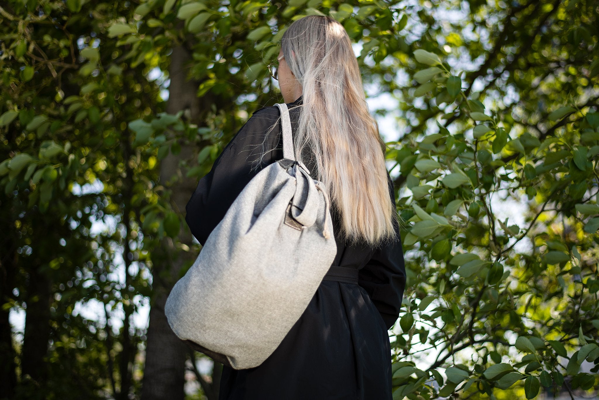 1. Woman wearing Trendbag Märss upcycled bag in light grey, shown outdoors with greenery