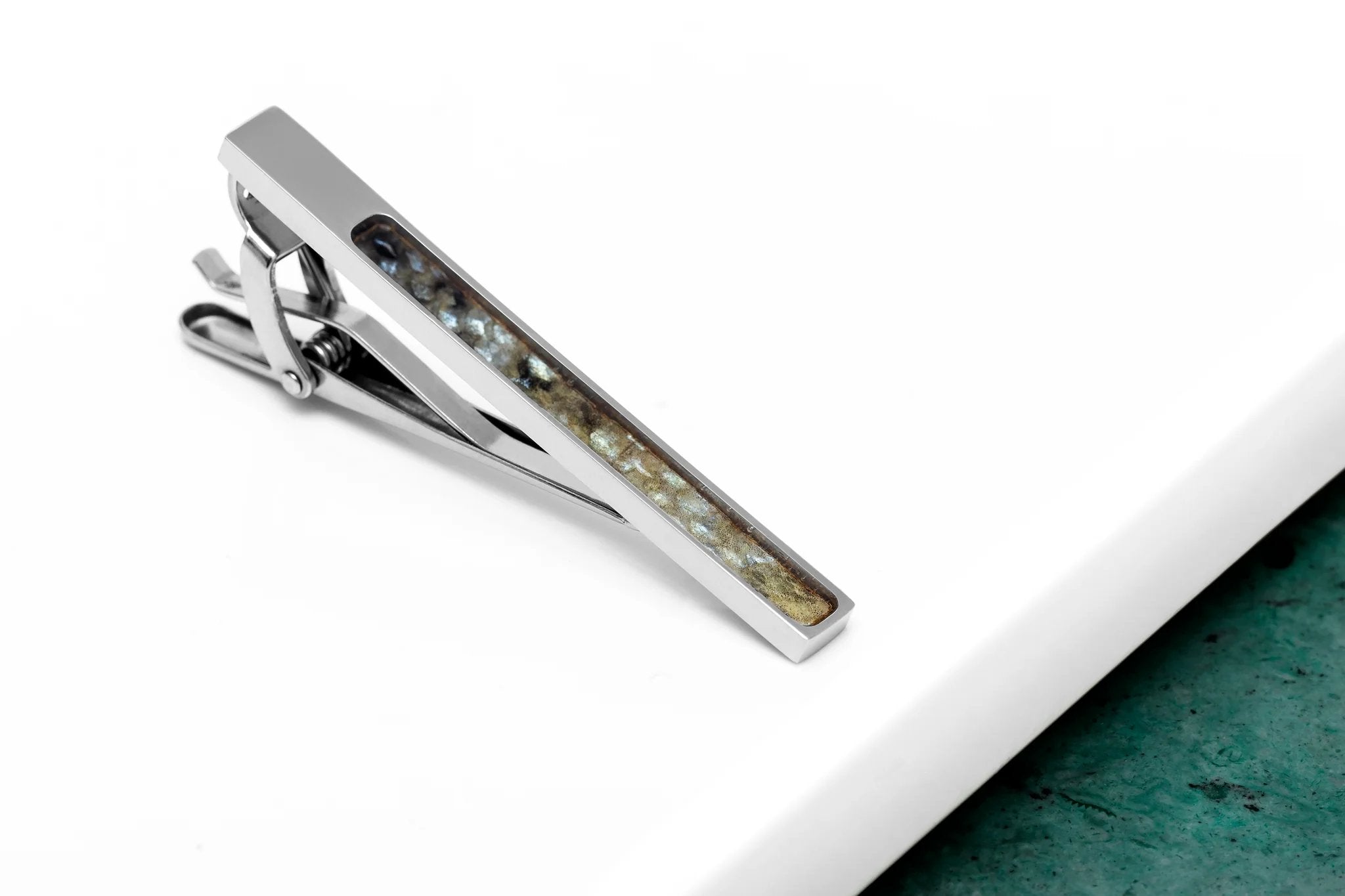 1. Black-spotted fish leather tie clip with stainless steel base on white and green surface