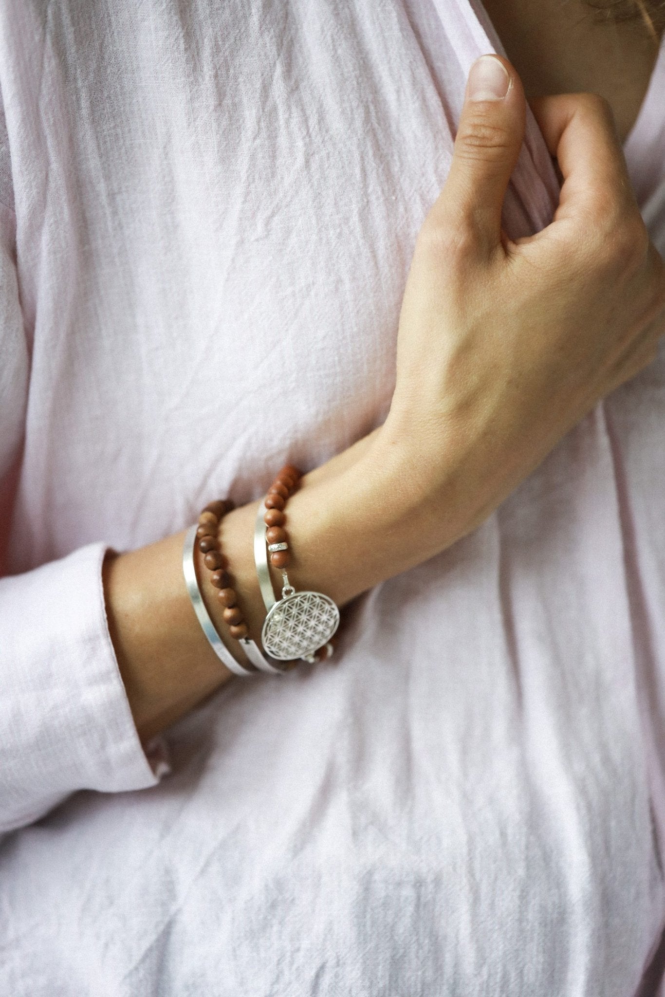 5. Close-up of woman wearing New Vintage by Kriss Flower Of Life Bracelet in sandalwood with 925 silver medallion, styled with additional bracelets