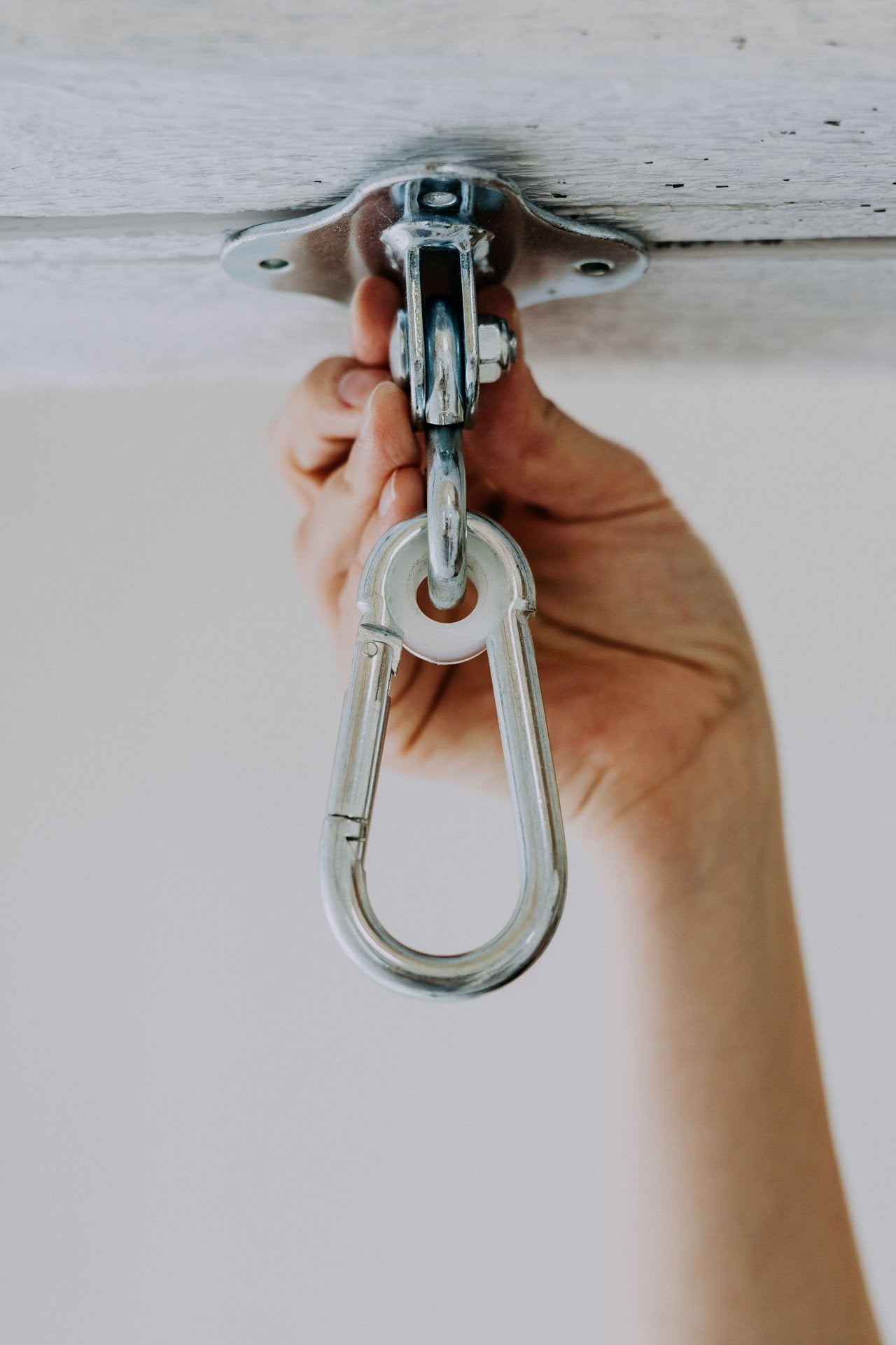 2. Hand holding installed HopOn Swing Hanger by Nofi KIDS on wooden ceiling