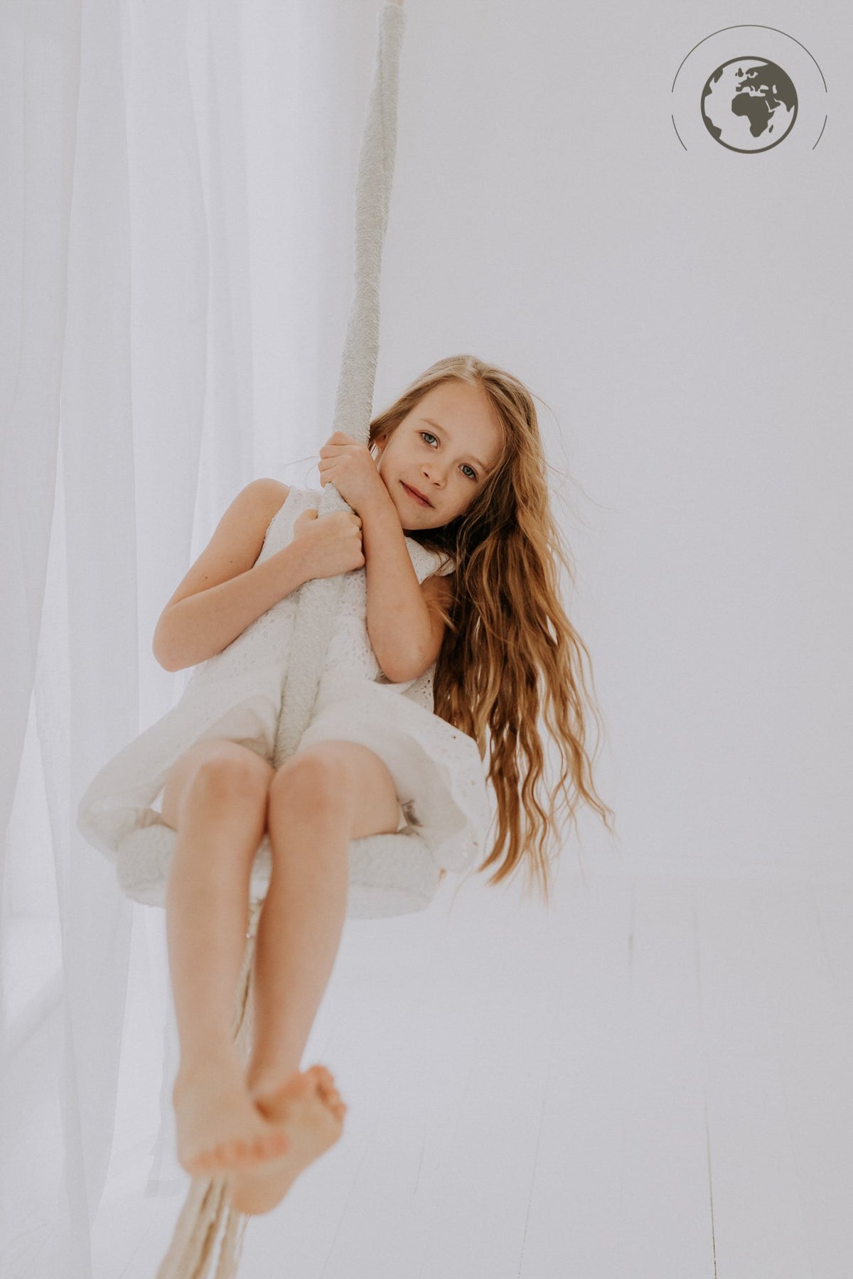1. Young girl in white dress swinging on ice grey bouclé swing in bright room
