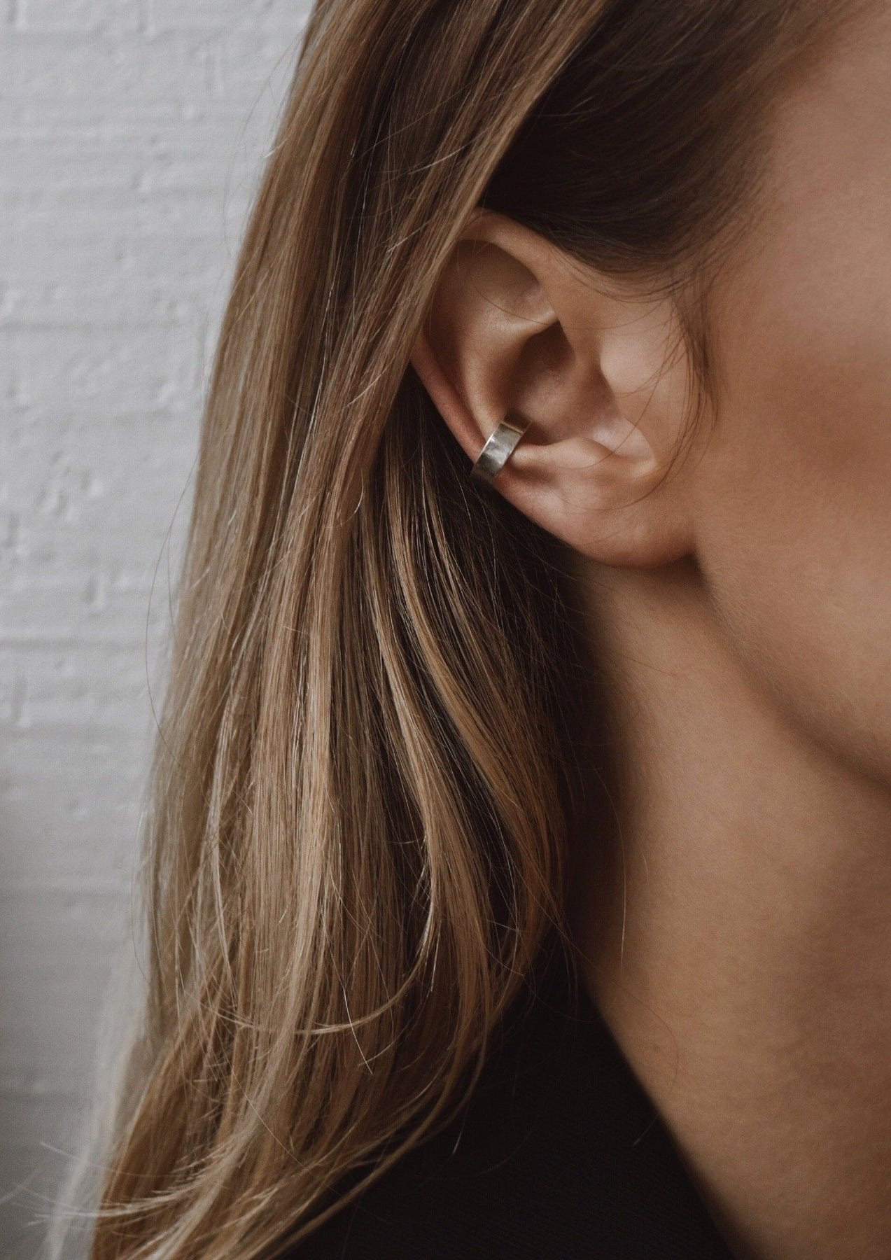 6. Close-up of NO MORE flat ear cuff in silver on woman's ear, highlighting its simple and elegant design