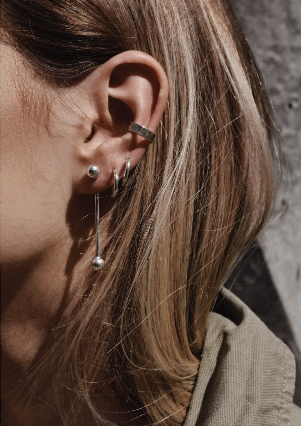 4. Close-up of woman's ear adorned with NO MORE flat ear cuff in silver, styled with multiple earrings for a layered look