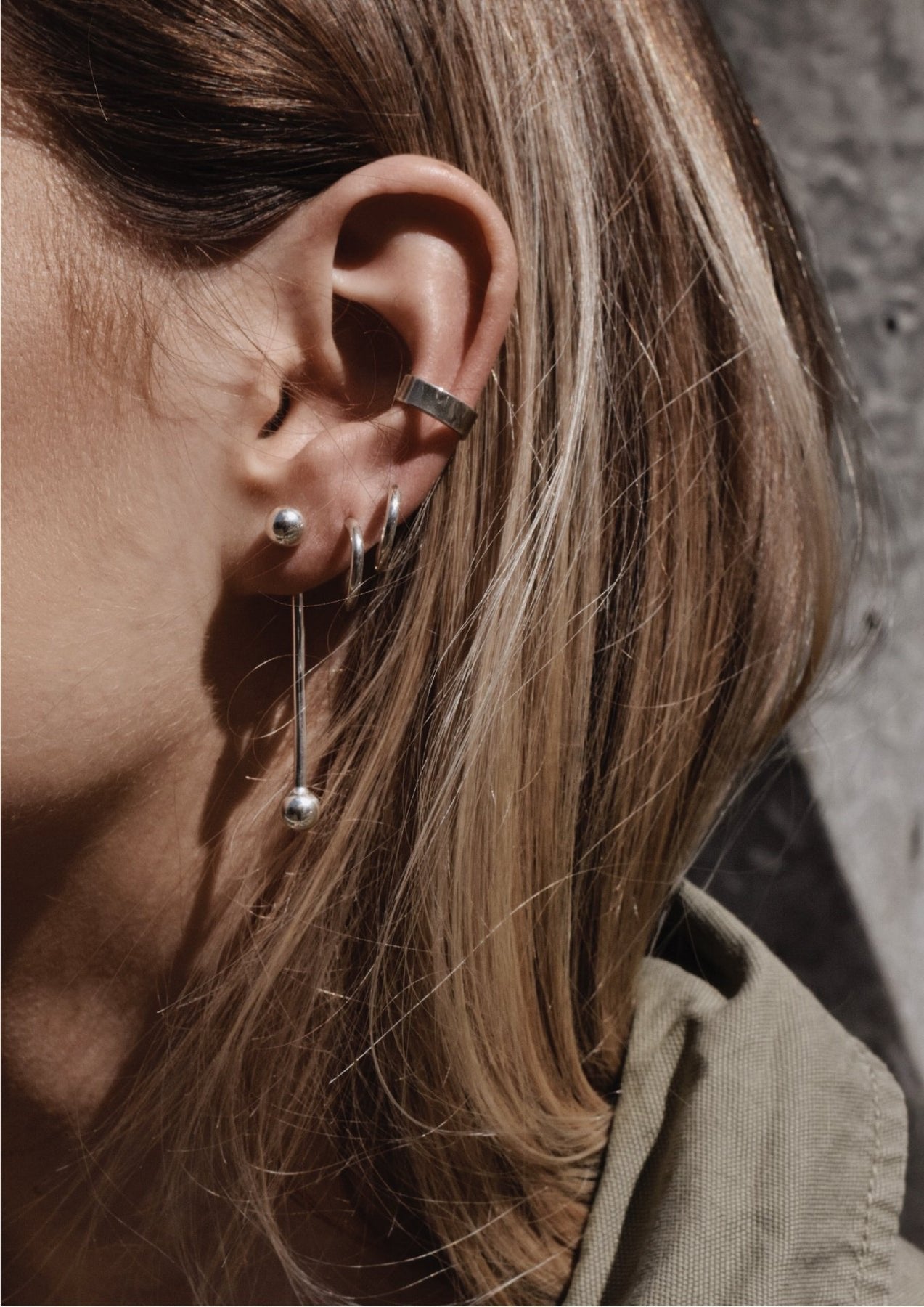 4. Close-up of woman's ear adorned with NO MORE flat ear cuff in silver, styled with multiple earrings for a layered look
