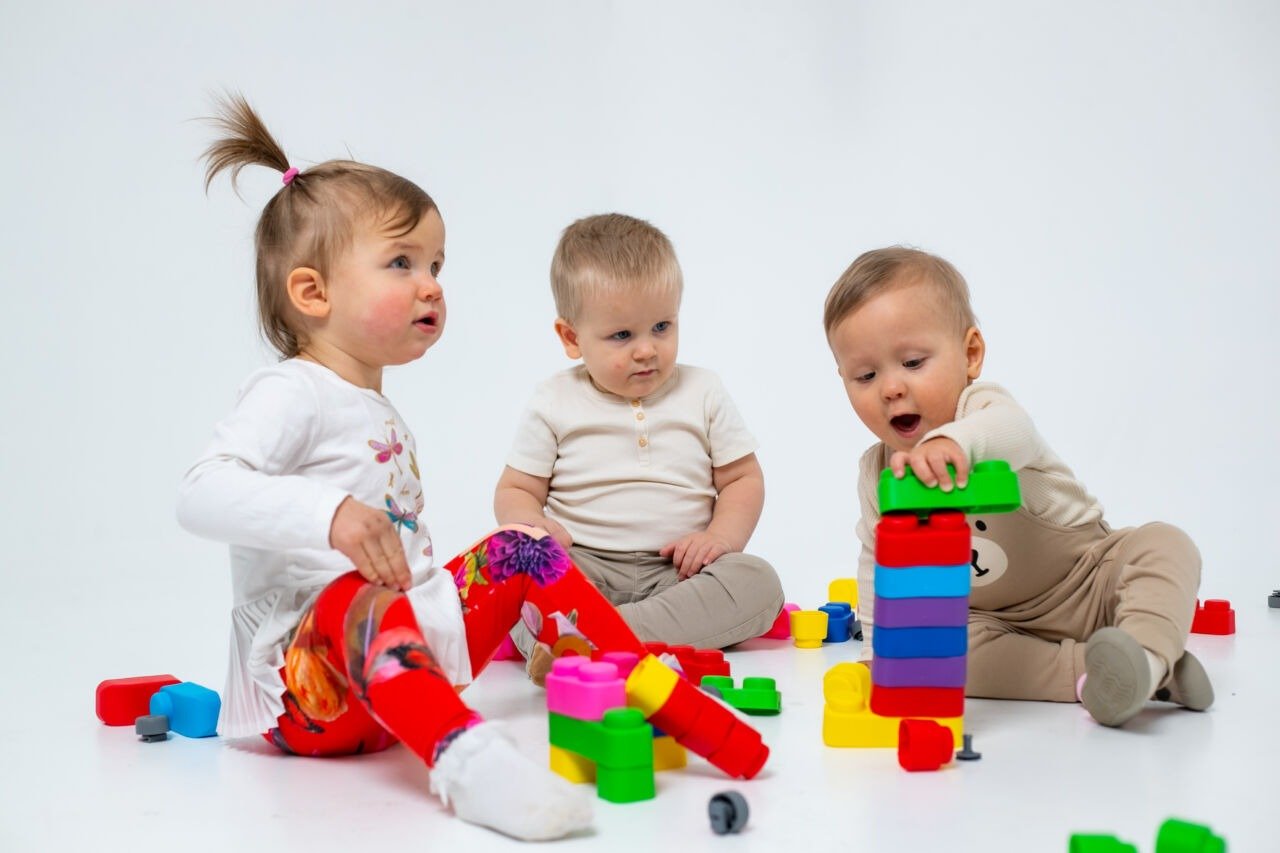 1. Three toddlers playing with colorful Gerardo's Toys soft blocks on a white background, enhancing creativity and motor skills