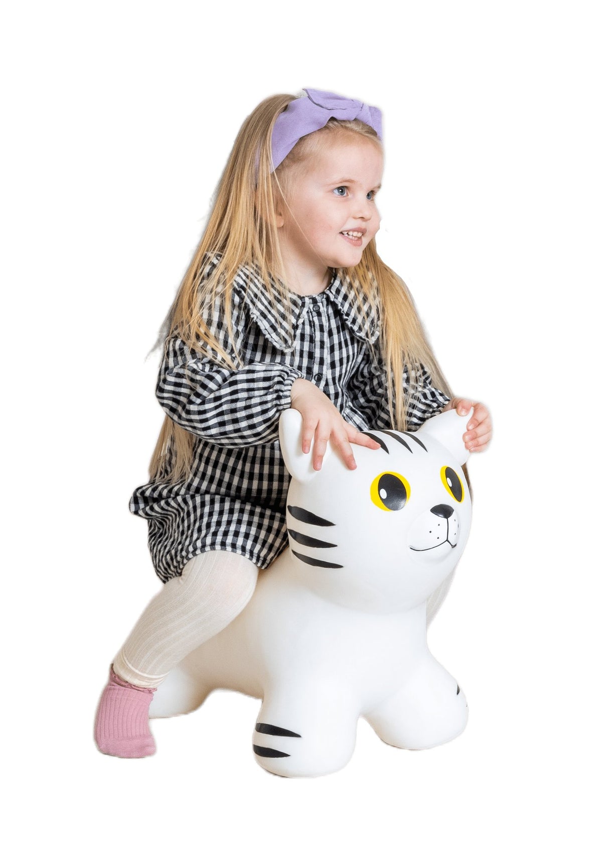 1. Young girl with long blonde hair sitting on white cat-shaped hopper toy with black stripes, wearing a checkered dress and pink socks, on a black background