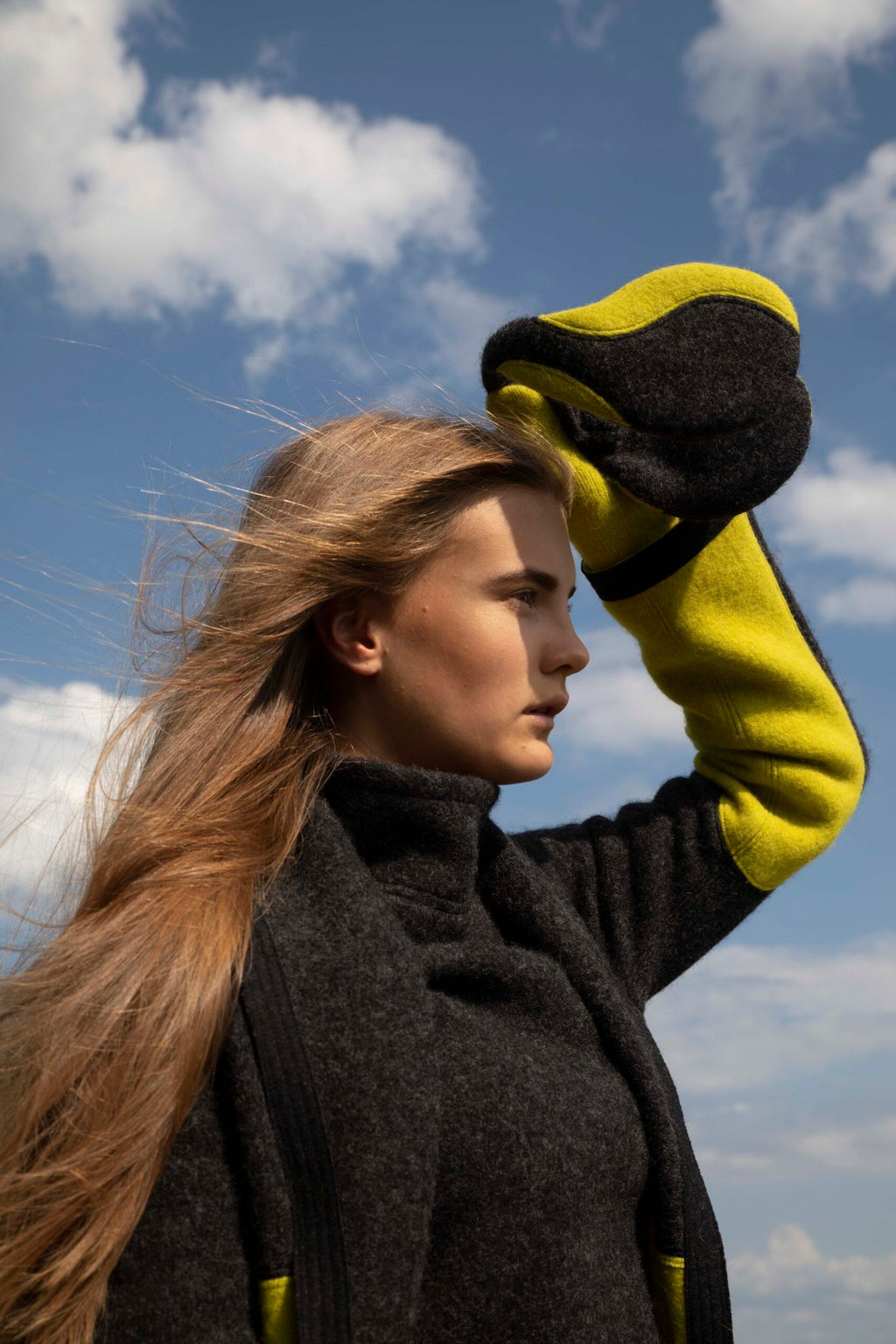 3. Side view of woman wearing HERTTA felted wool earmuffs in dark grey and apple green, outdoor lifestyle setting