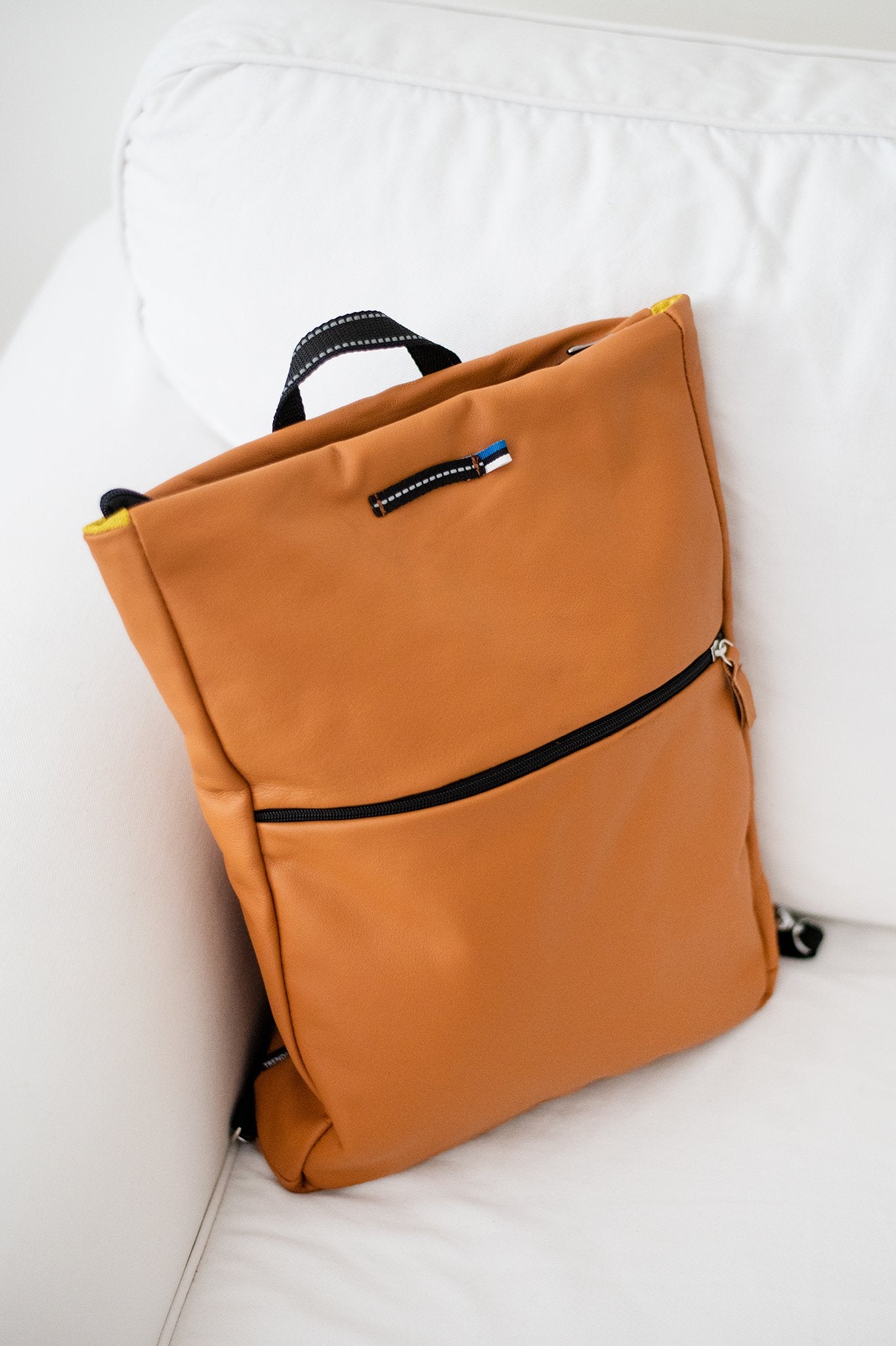 2. Trendbag Barbara Leather Backpack in Calvados on white sofa, showcasing front zippered pocket