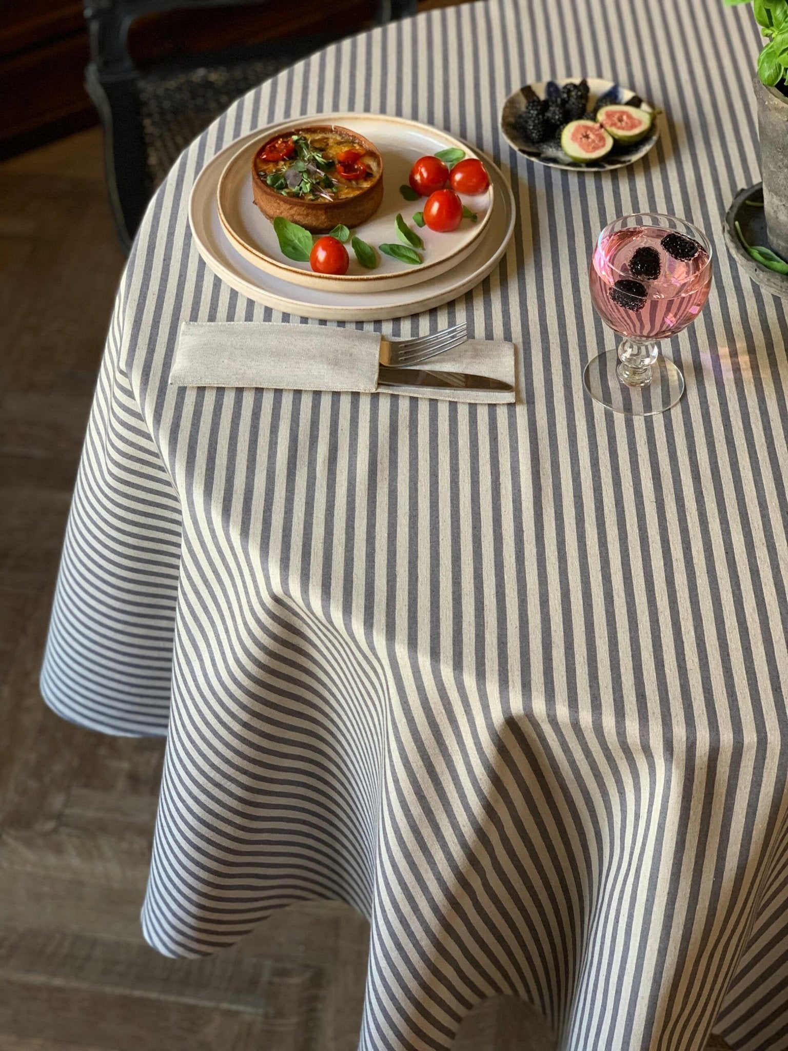 1. Round table with Hortensias Home tablecloth in beige with blue lines, set with food and drink, showcasing Nordic country style