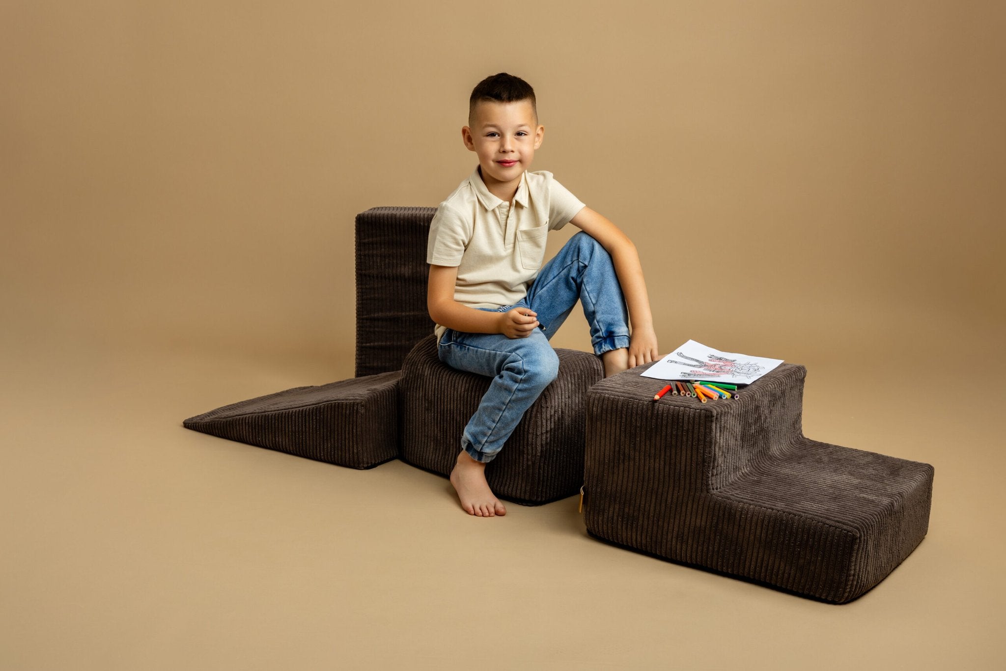 4. Boy sitting on brown play set with coloring book and crayons, smiling on beige background