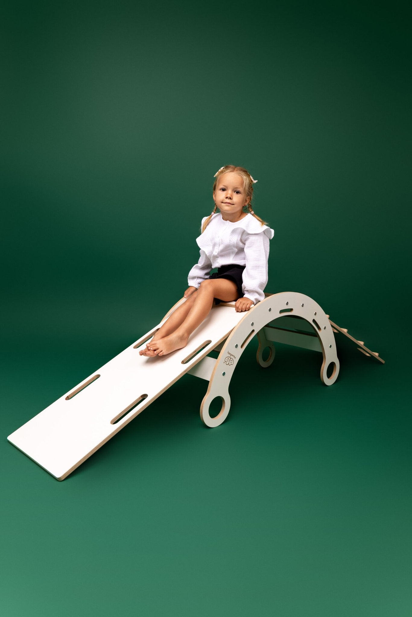 1. Child sitting on white wooden dream rocker with slide and ladder against green background
