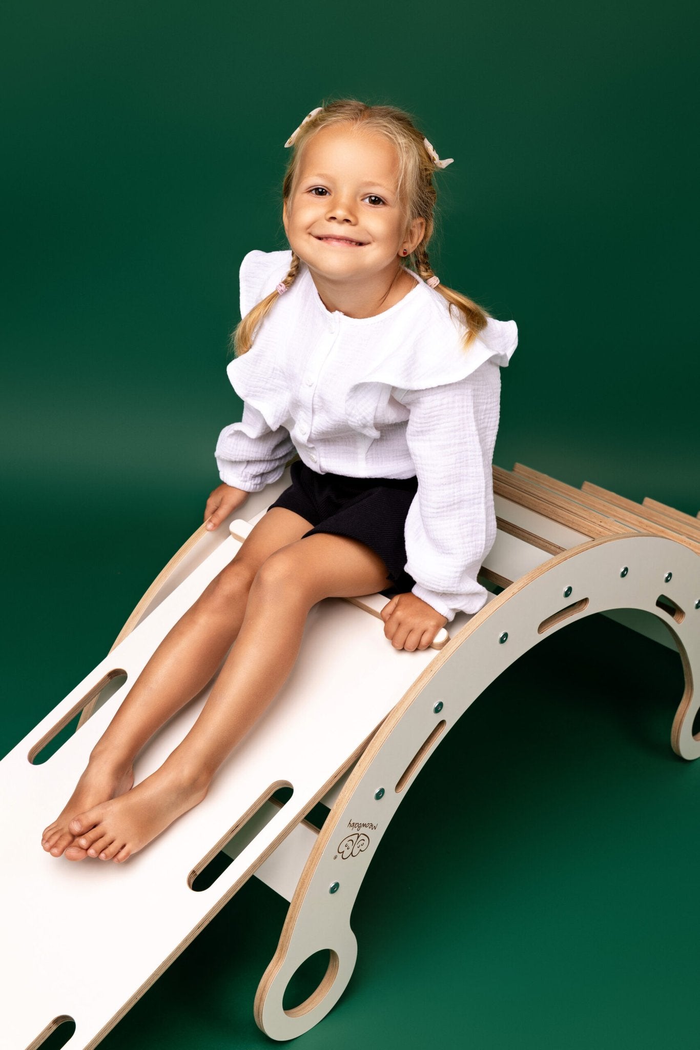 1. Smiling child sitting on white wooden dream rocker with slide in front of green background