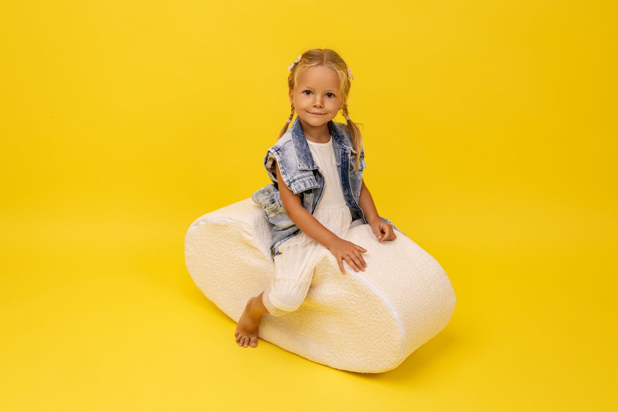 1. Girl sitting on white boucle bean-shaped foam module by MeowBaby against yellow background