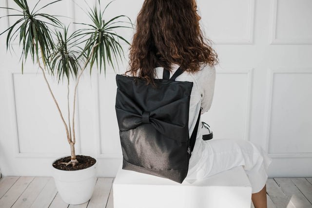 1. Woman sitting with Muni Black Bow Large waterproof backpack, showcasing stylish design and adjustable straps