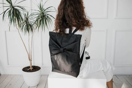 1. Woman sitting with Muni Black Bow Large waterproof backpack, showcasing stylish design and adjustable straps