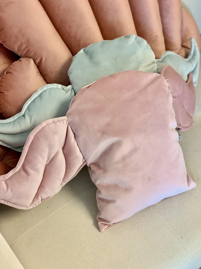 1. Child sitting on a bed with a dusty pink decorative cushion with wing design, surrounded by illustrated pillows in a cozy room