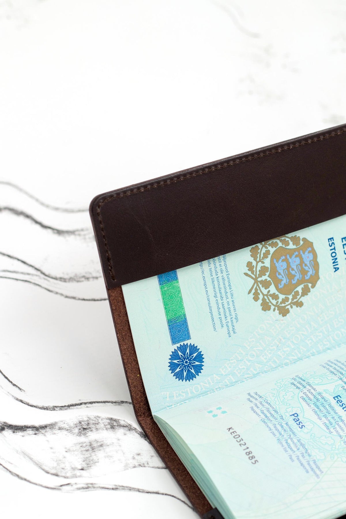 1. Open passport in dark brown leather cover by Stella Soomlais on white background with abstract lines