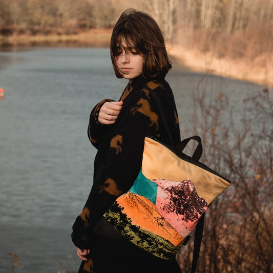 1. Woman by a lake wearing Muni Bold Mountains backpack with colorful mountain print