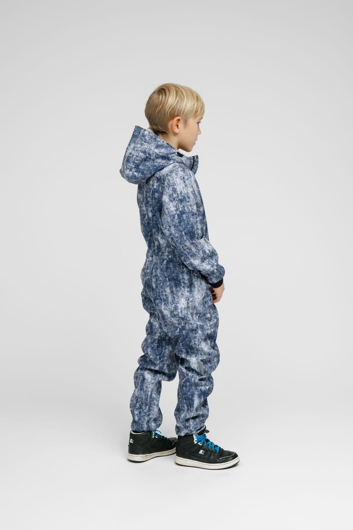 4. Child in blue patterned softshell onesie with hood and black sneakers shown from side in studio