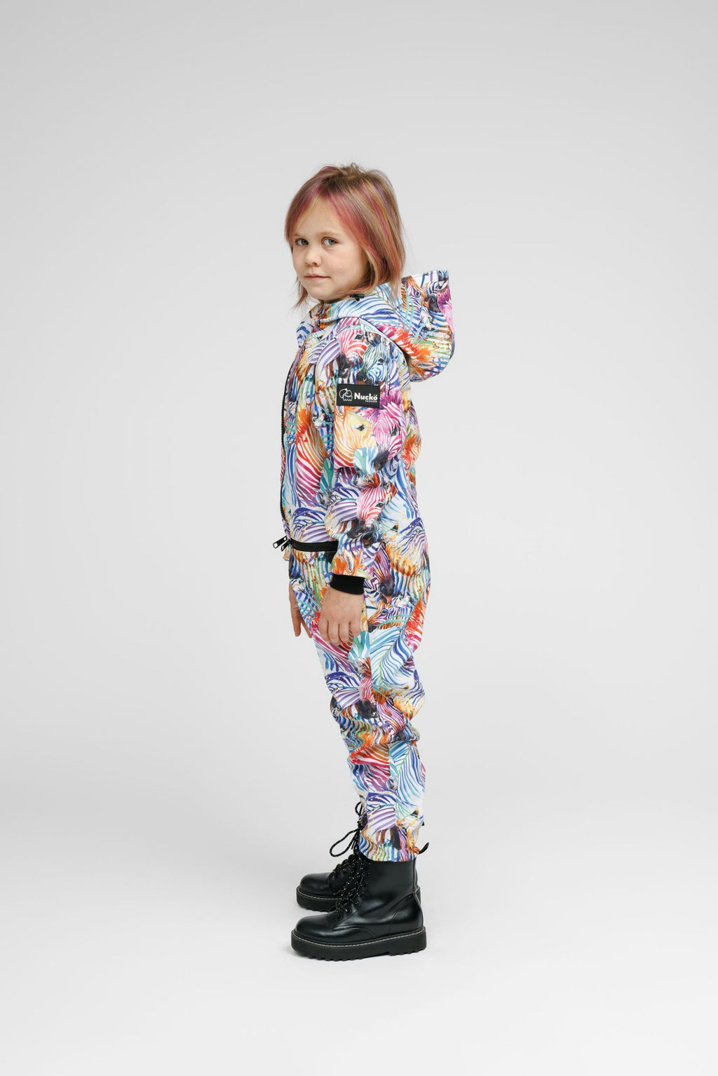 5. Side profile of child in Nuckö rainbow softshell onesie with hood, studio background