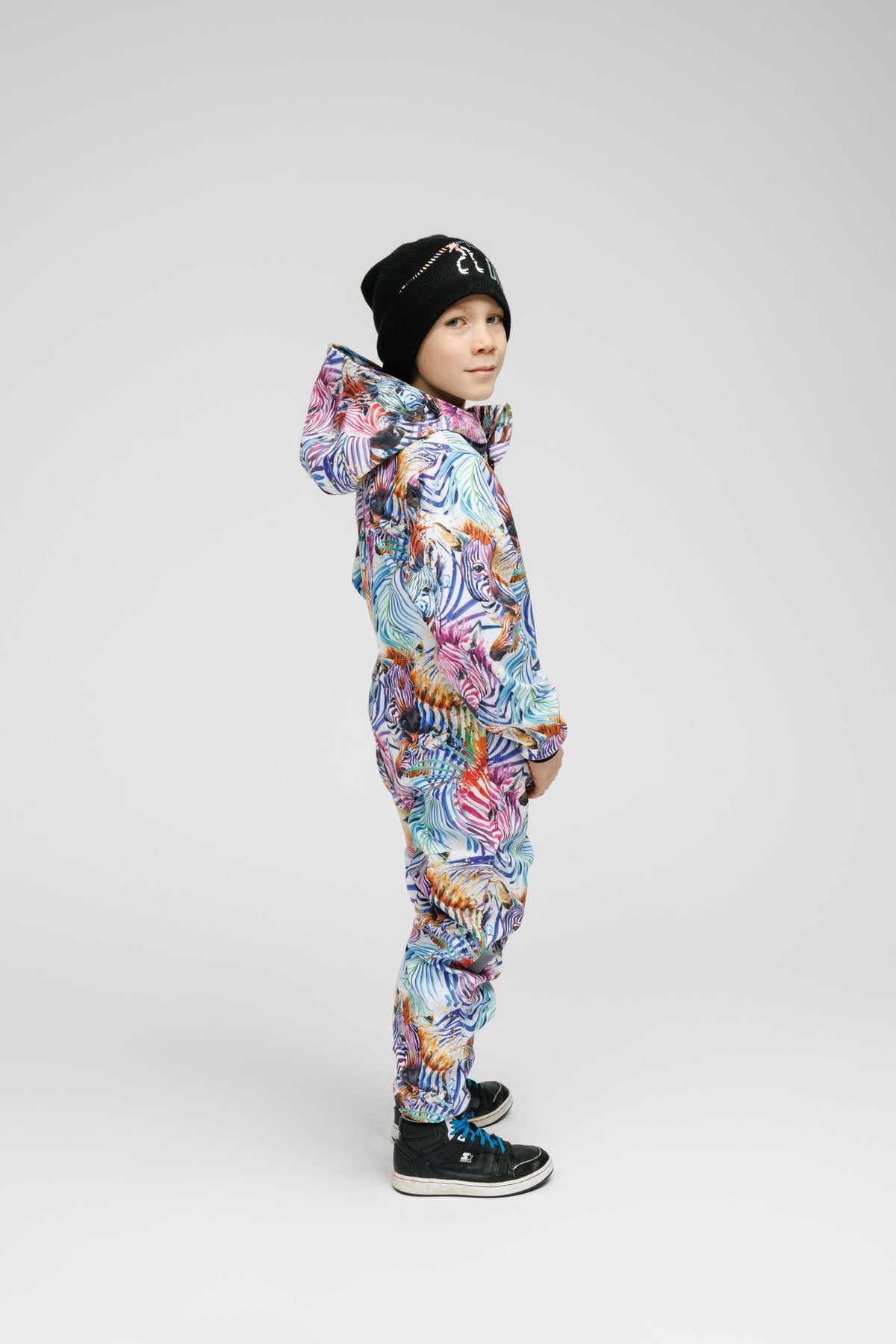 8. Side view of child in Nuckö rainbow softshell onesie with black beanie, studio background